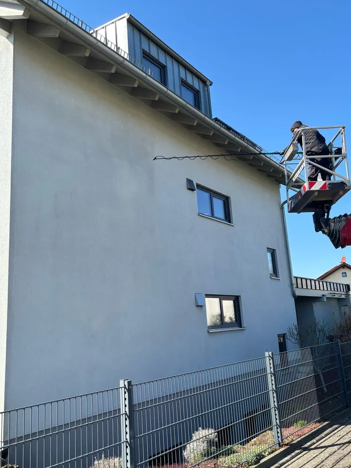 Mitarbeiter reinigt eine graue Putzfassade von der Hebebühne aus